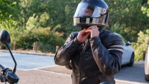 A person putting on a black motorcycle helmet.