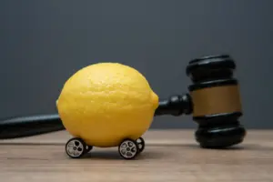 A lemon with small wheels attached, next to a gavel.