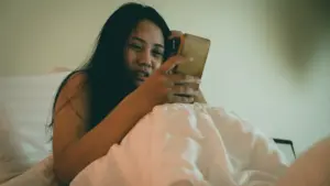 A distraught woman looking at her phone while in bed.